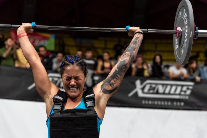 Athletic girl lifting a barbell above her head, with an expression of concentration and effort on her face.