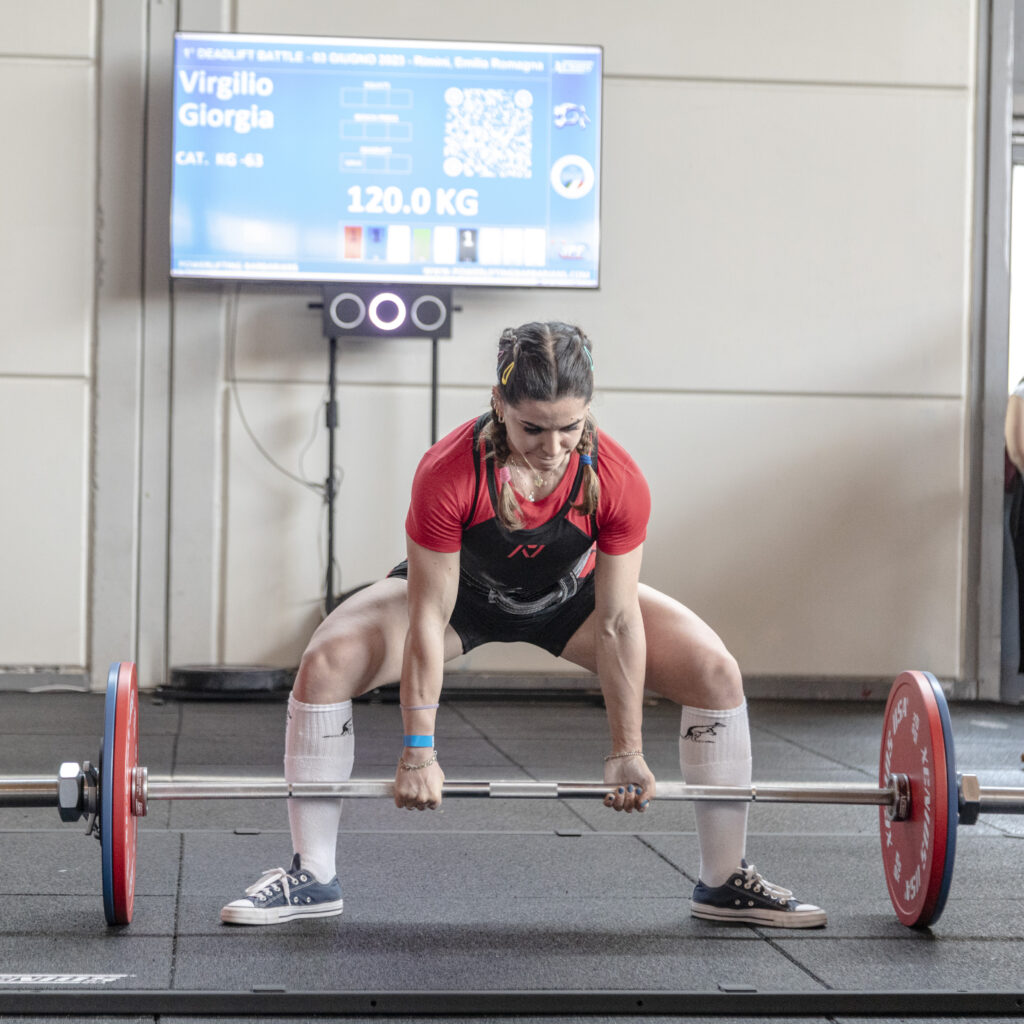 athlete girl in position to start making a break from the ground during a competition: behind her in fact are reported his data as the name, the pounds he is going to lift and the category